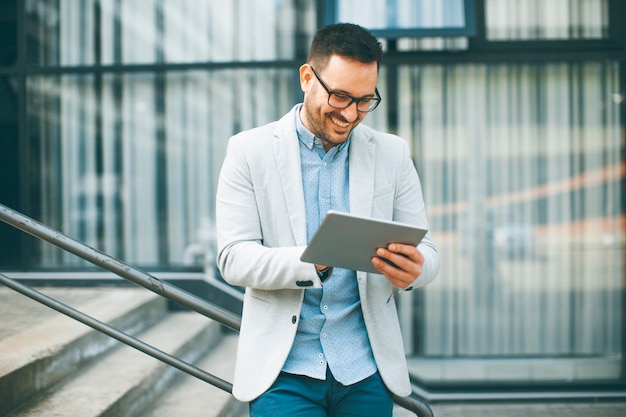 Beau jeune homme d&#39;affaires avec tablette numérique par l&#39;immeuble de bureaux