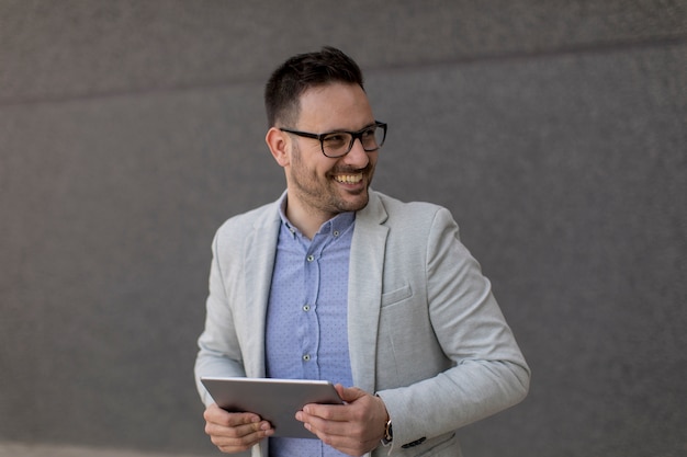 Beau jeune homme d&#39;affaires avec tablette numérique par le mur gris