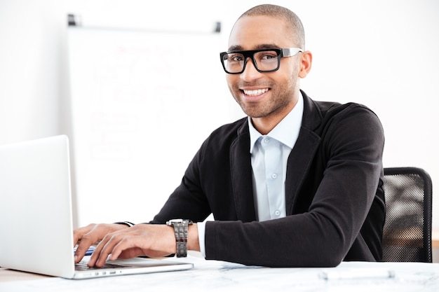 Beau jeune homme d'affaires travaillant avec des documents et un ordinateur portable au bureau