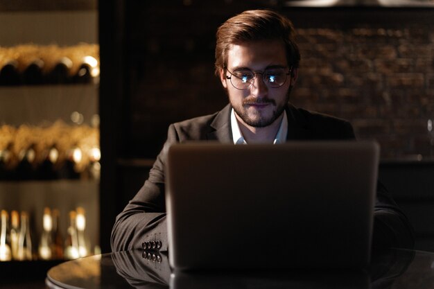 Beau jeune homme d'affaires travaillant sur un ordinateur portable à son bureau tard dans la nuit.