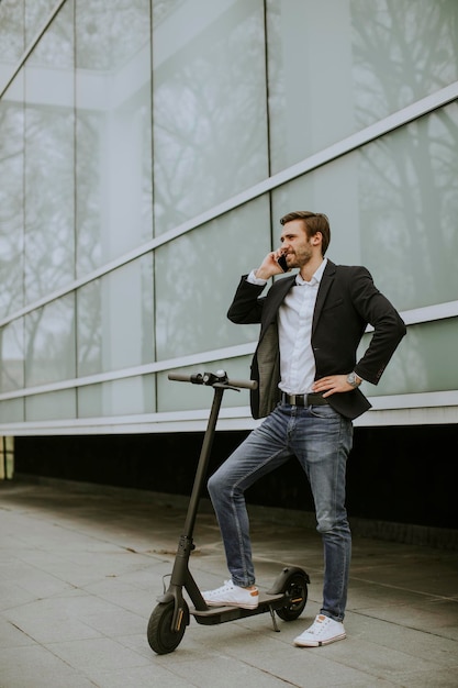 Beau jeune homme d'affaires utilisant un téléphone portable sur un scooter électrique