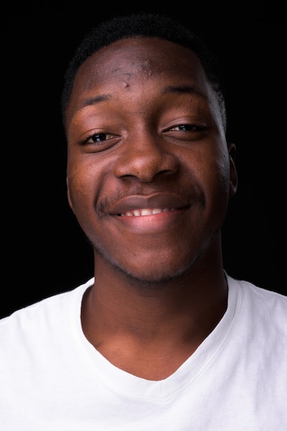 Beau jeune homme africain aux cheveux afro contre le mur noir