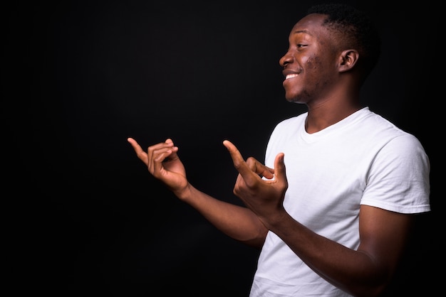 Beau jeune homme africain aux cheveux afro contre le mur noir