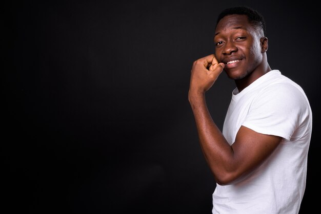 Beau jeune homme africain aux cheveux afro contre le mur noir