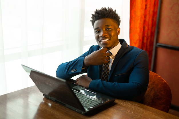 Beau jeune homme africain en costume à l'intérieur avec ordinateur portable