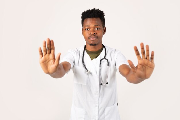 Beau jeune homme africain sur fond blanc en robe médicale avec le geste de la main