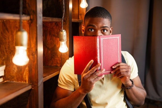 Photo beau jeune homme africain lisant un livre dans la bibliothèque