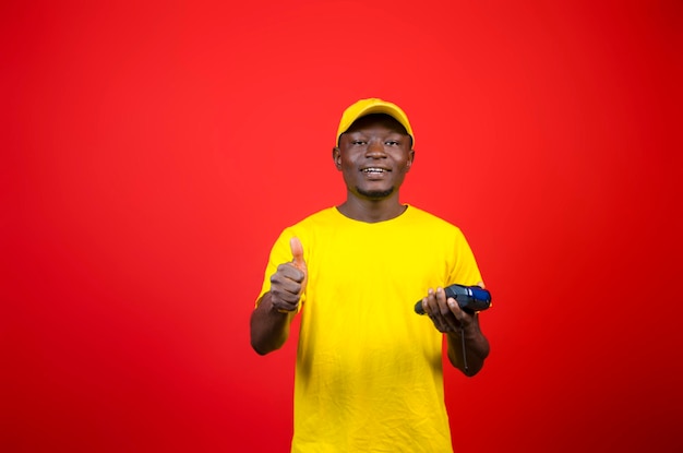 Un beau jeune homme africain portant un tissu jaune se sentant excité alors qu'il tient sa machine de point de vente