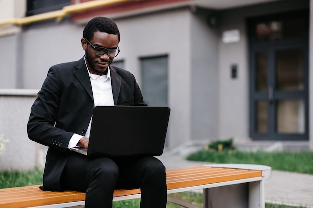 Beau jeune homme afro-américain travaillant sur ordinateur portable assis o