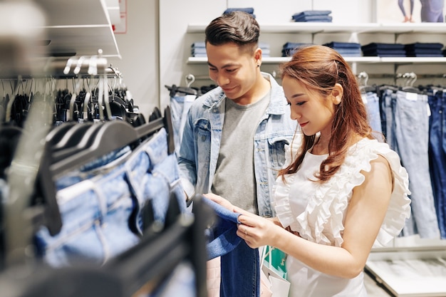 Beau jeune homme aidant sa petite amie à choisir les meilleurs jeans de la boutique