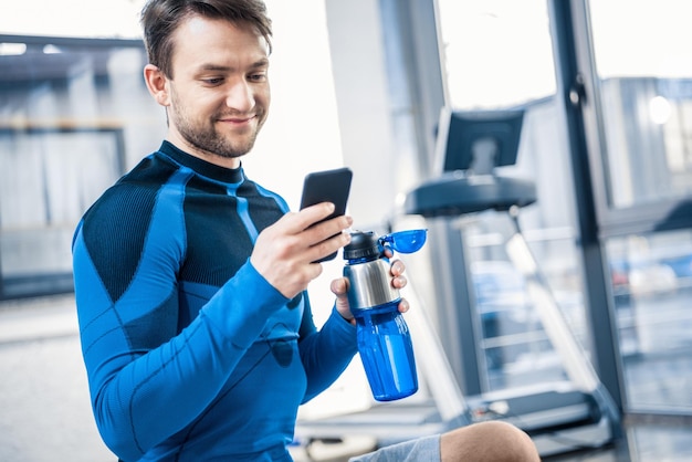 Beau jeune homme à l'aide de smartphone au gymnase