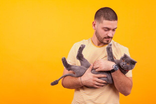 Beau jeune homme aimant et tenant son chat en studio sur fond jaune.