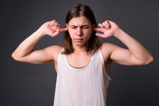 Beau jeune homme androgyne aux cheveux longs contre le mur gris