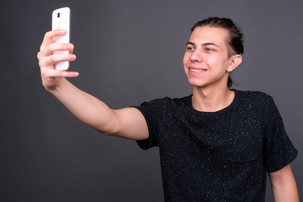 Beau jeune homme androgyne aux cheveux longs contre le mur gris