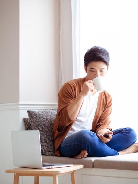 Beau jeune homme asiatique buvant à la maison