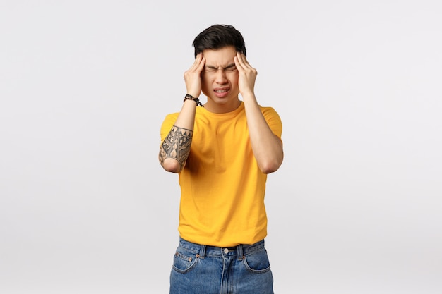 Beau jeune homme asiatique en t-shirt jaune avec maux de tête