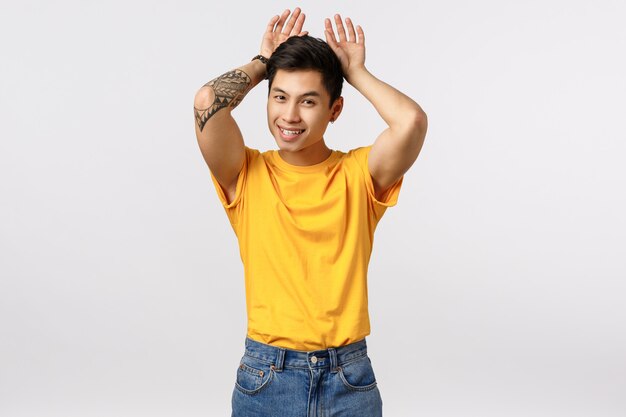 Beau jeune homme asiatique en t-shirt jaune montrant des oreilles de lapin avec les mains sur la tête