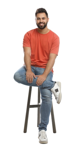 Beau jeune homme assis sur un tabouret sur fond blanc