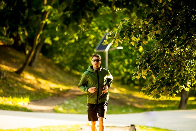 Beau jeune homme athlétique en cours d'exécution tout en faisant de l'exercice dans le parc verdoyant ensoleillé