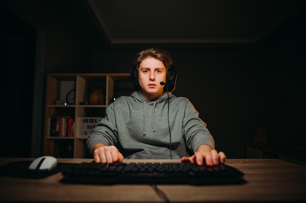 Beau jeune homme au casque sur la tête jouant à des jeux vidéo à la maison sur l'ordinateur