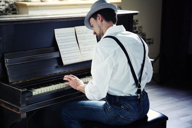 Beau jeune homme au chapeau faisant de la musique pour piano