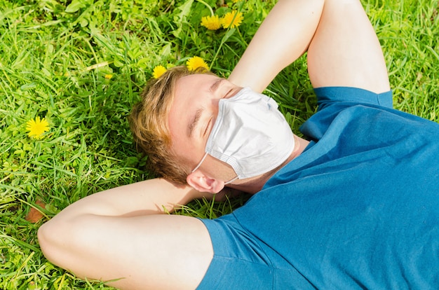 Beau jeune homme au visage masque médical se trouve sur l'herbe verte