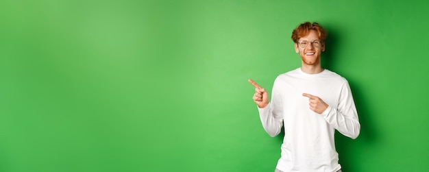 Beau jeune homme aux cheveux rouges et à la barbe souriant pointant du doigt le logo montrant la publicité