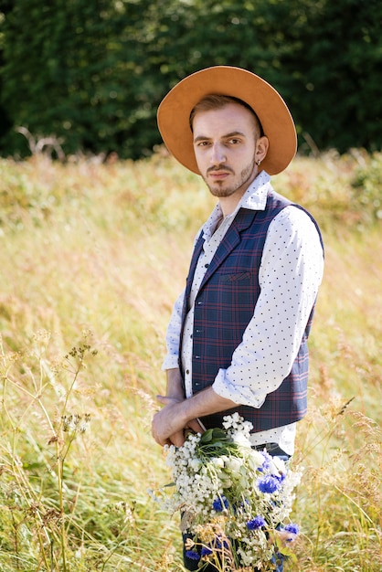 Un beau jeune homme avec une barbe et un chapeau sur le terrain avec un bouquet de fleurs