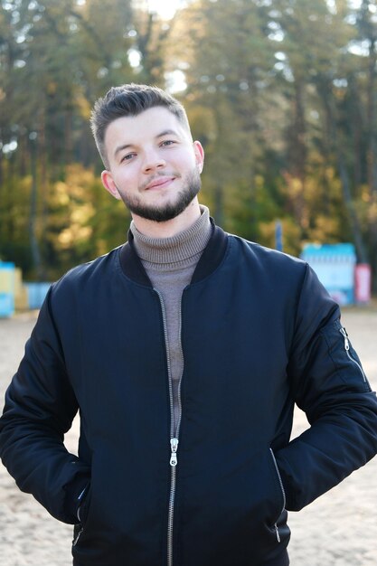 Beau jeune homme avec une barbe et une veste noire posant sur la plage Slow living Appréciant les petites choses Lykke concept