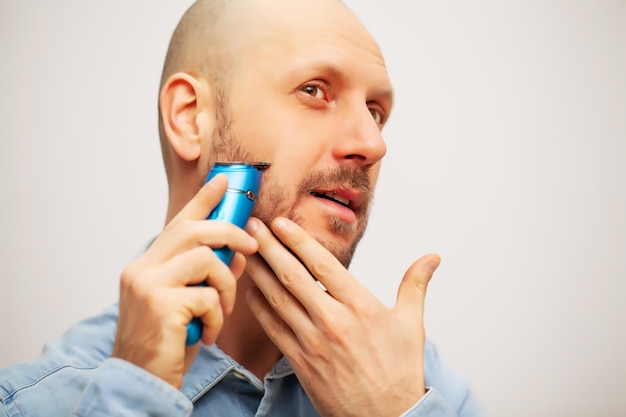 Beau jeune homme barbu taillant sa barbe avec une tondeuse