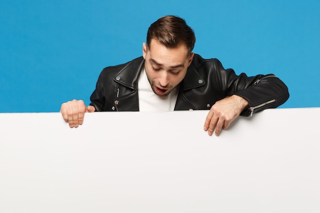 Beau jeune homme barbu tient un grand panneau d'affichage vide blanc pour le contenu promotionnel isolé sur un portrait de studio de fond de mur bleu. Concept de mode de vie des émotions sincères des gens. Maquette de l'espace de copie.