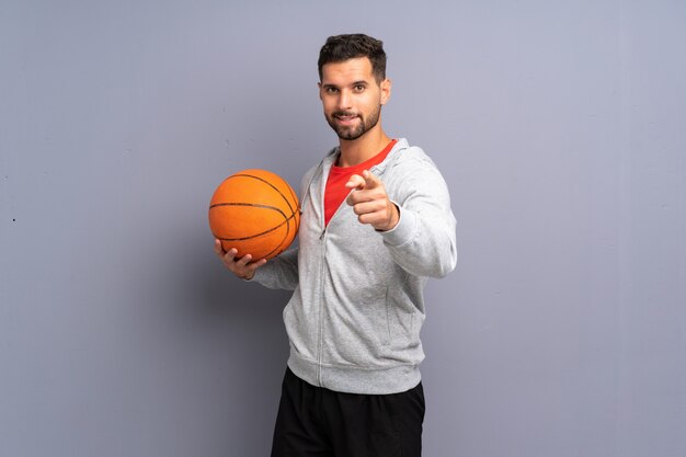 Beau jeune homme de basket-ball pointe le doigt vers vous avec une expression confiante