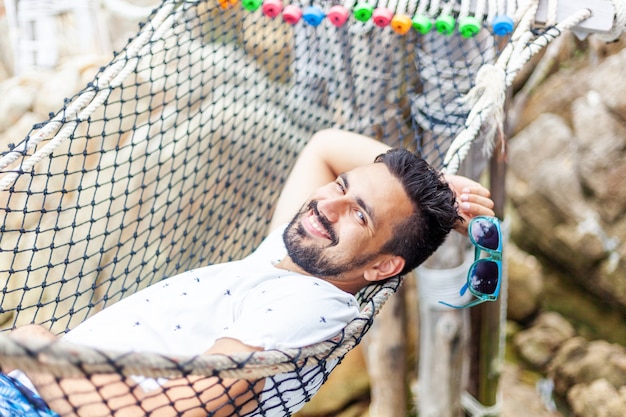 Beau jeune homme brune latine séduisante à lunettes de soleil avec une barbe sur un hamac en vacances