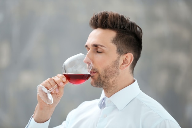 Beau jeune homme buvant du vin rouge à l'intérieur