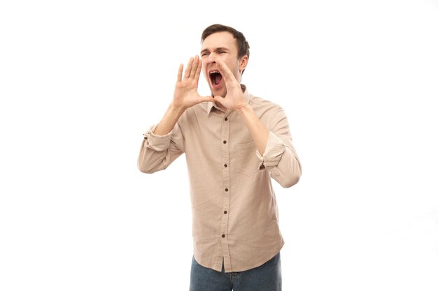 Beau jeune homme caucasien heureux criant et tenant les mains autour de la bouche isolée sur fond de studio blanc. Attention aux nouvelles excitées !