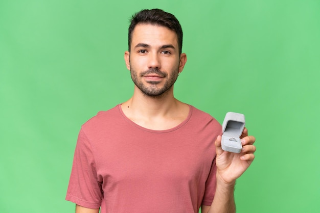 Beau jeune homme caucasien tenant une bague de fiançailles sur fond isolé souriant beaucoup