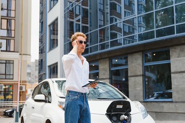 Un beau jeune homme charge sa voiture électrique moderne.