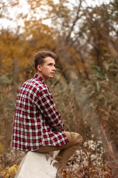 Beau jeune homme en chemise à carreaux assis dans la nature un jour d'automne