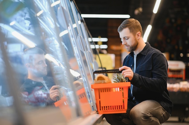 Beau jeune homme choisissant de la nourriture au supermarché