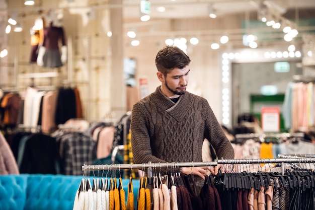 Un beau jeune homme en choisissant des vêtements dans un magasin de détail