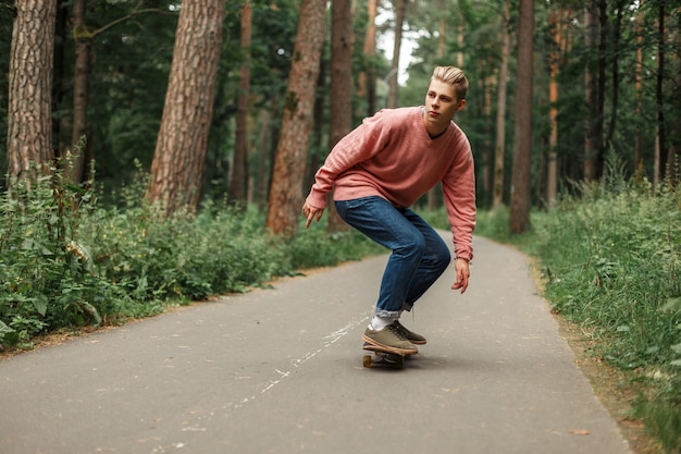 Beau jeune homme avec une coiffure à cheval sur une planche à roulettes dans le parc