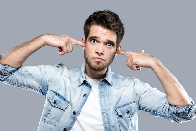 Beau jeune homme couvrant ses oreilles sur fond gris.