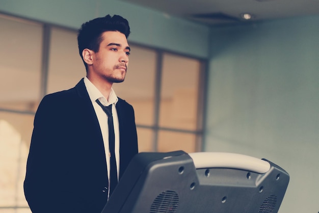 Beau jeune homme dans un costume noir chemise blanche et cravate sur un tapis roulant dans la salle de gym