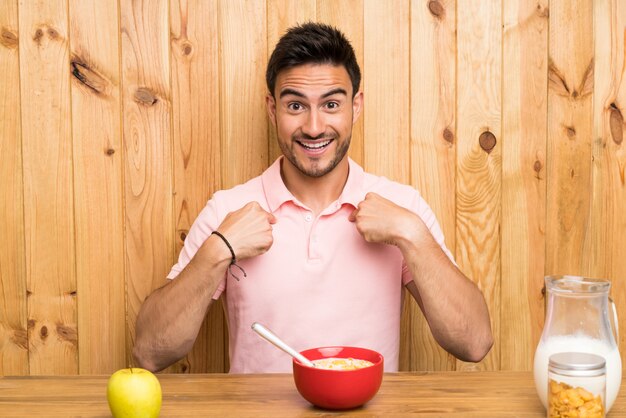 Beau jeune homme dans une cuisine prenant son petit déjeuner avec une expression faciale surprise