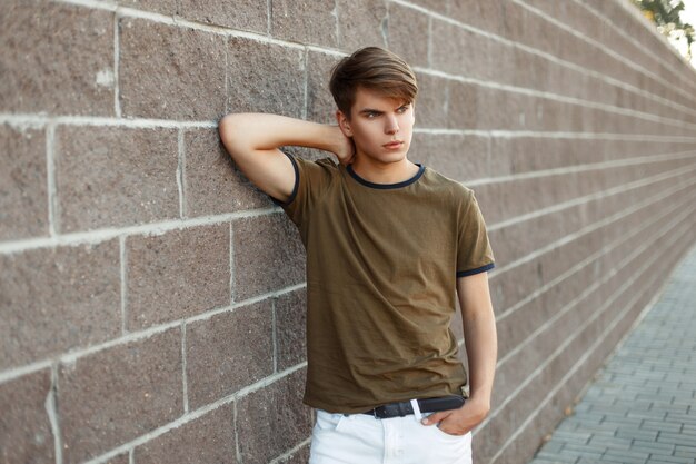 Beau jeune homme dans un T-shirt près d'un mur de briques