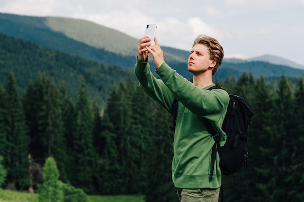 Beau jeune homme debout dans les montagnes avec un smartphone surélevé et à la recherche d'une connexion cellulaire avec un visage sérieux Manque d'internet dans les montagnes