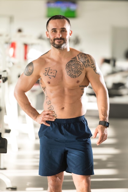 beau, jeune homme, debout, fort, dans, les, gymnase, et, flexion, muscles, musclé, athlétique, bodybuilder, forme physique, modèle, poser, après, exercices