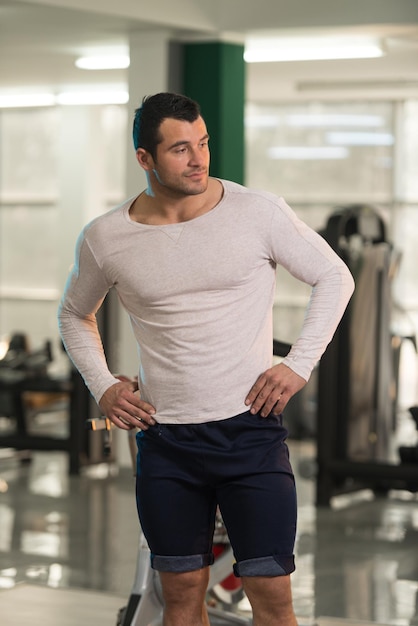 Beau jeune homme debout fort en t-shirt blanc et muscles fléchissants Muscular Athletic Bodybuilder Fitness Model Posing After Exercises