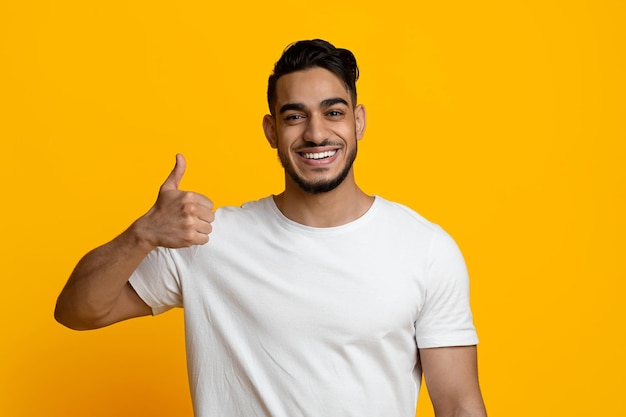 Beau jeune homme du Moyen-Orient montrant le pouce vers le haut sur jaune