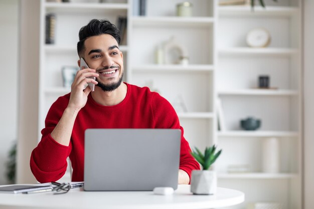 Beau jeune homme du Moyen-Orient parlant sur téléphone portable au bureau à domicile